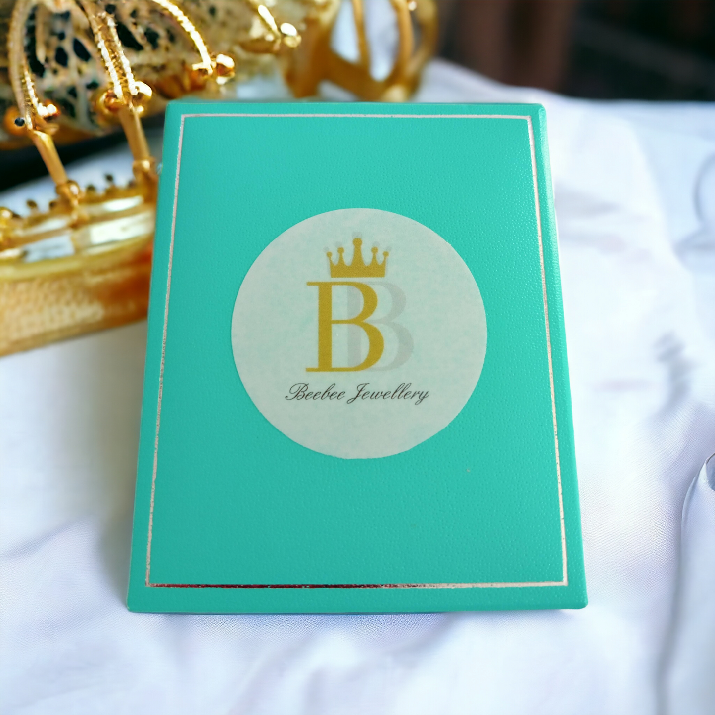 Beebee Jewellery turquoise box on a white fabric with a gold crown in the left corner