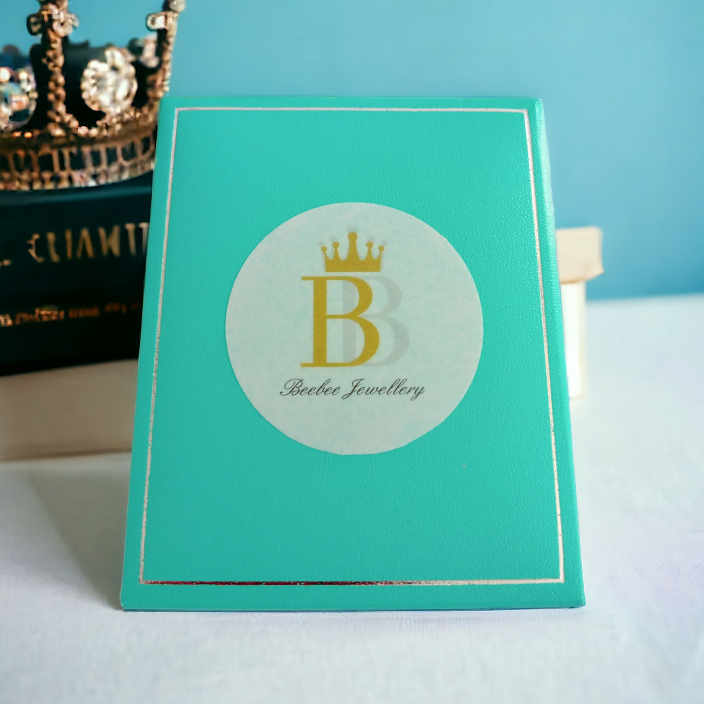 Turquoise jewellery box with a white and blue background, books and a crown in the background.