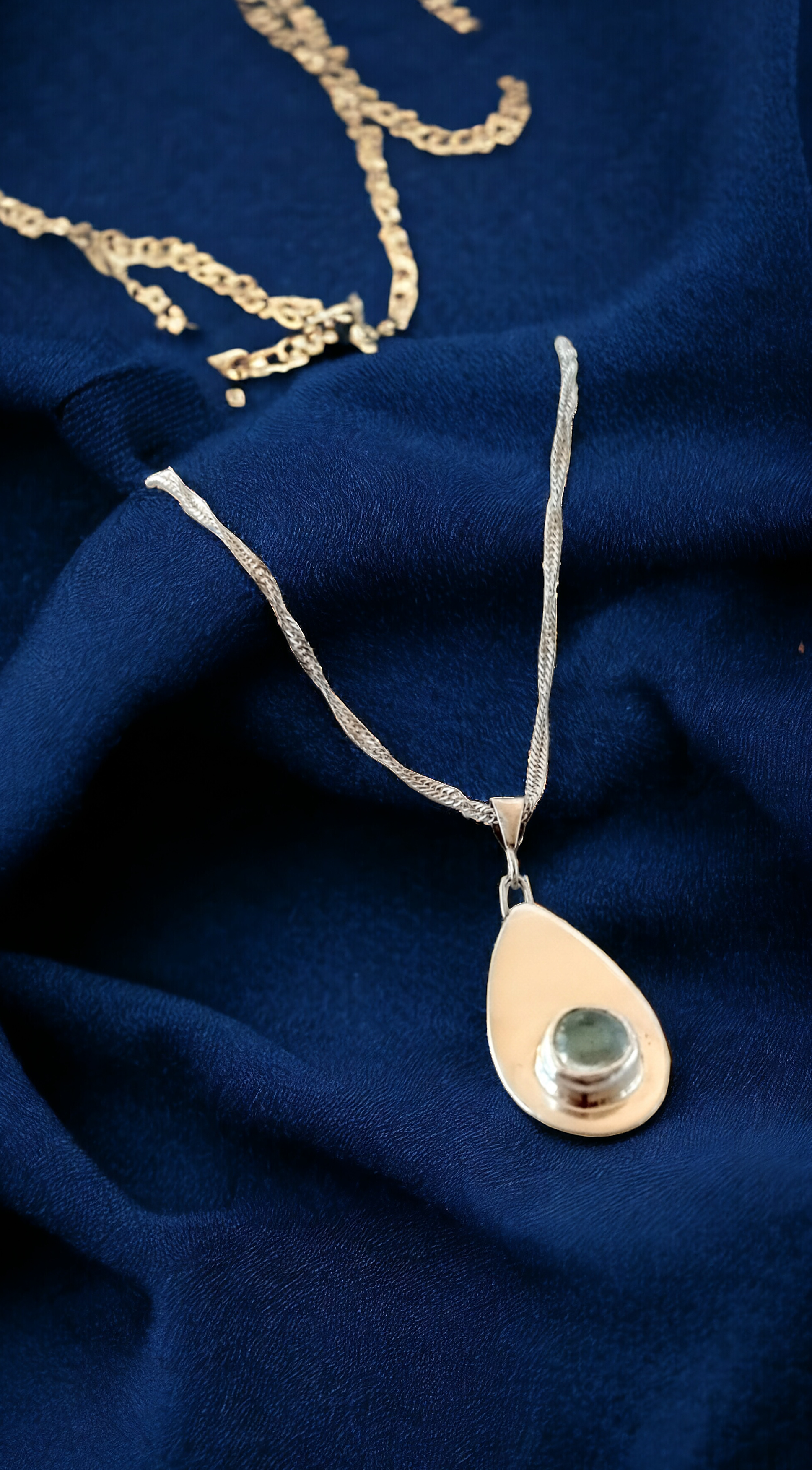 Silver teardrop pendant with blue topaz on a blue fabric background