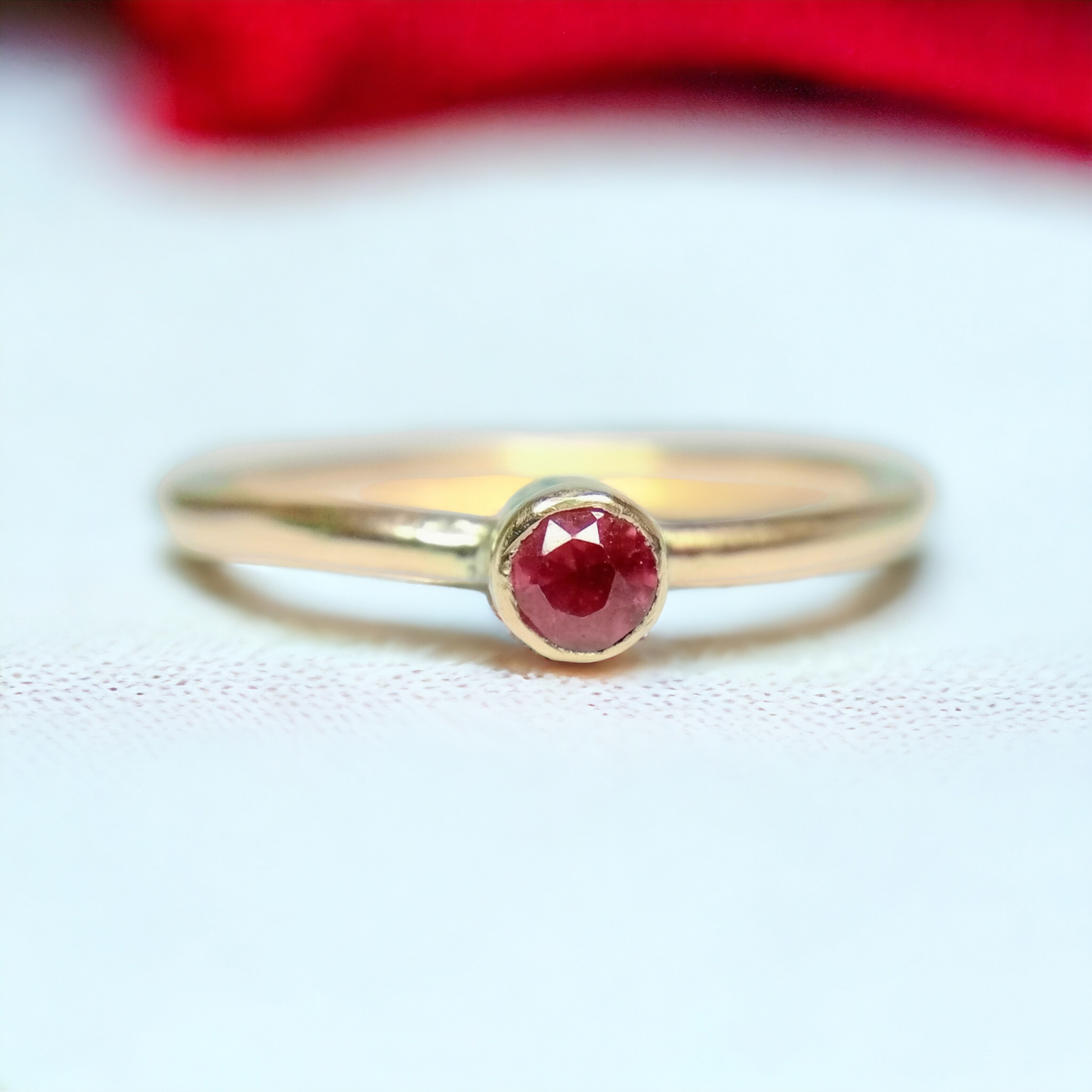 gold ruby solitaire ring on a white canvas with a red fabric in the background