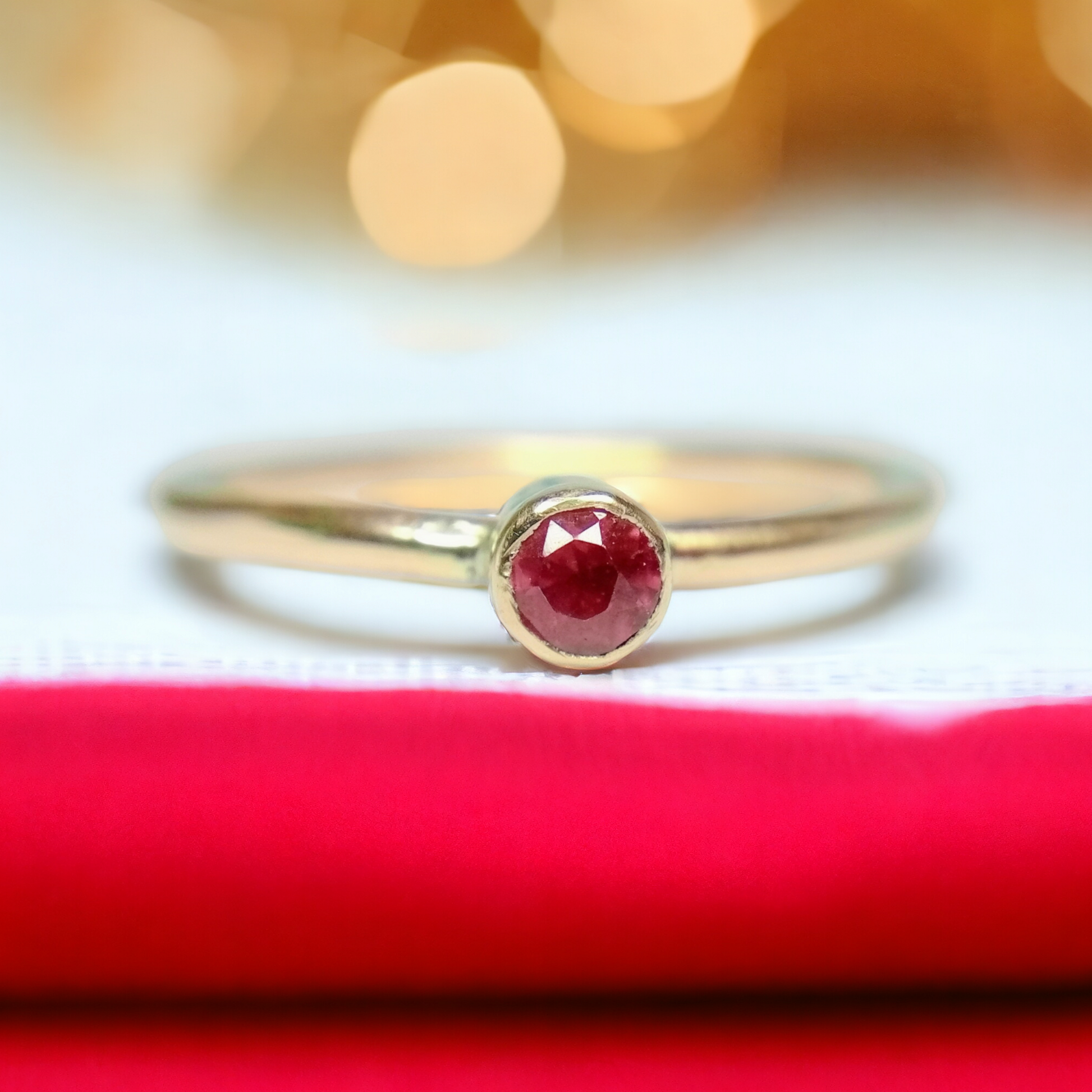 Gold ruby ring with red stone on a red and white fabric with blurred lights in the background