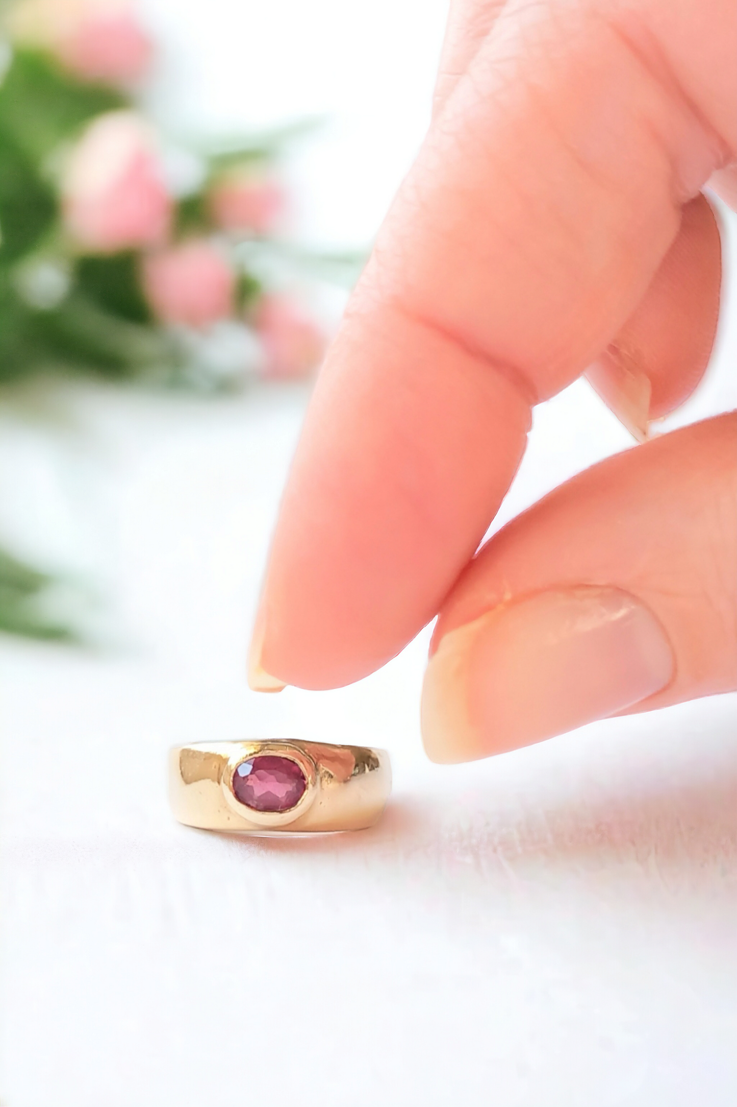 Gold and garnet ring on a silk fabric with a hand picking up the ring